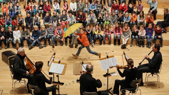 Fünf Musiker auf Bühne, Kinder und Publikum und eines rennend mit einem Regenschirm. © NDR Foto: Marcus Krüger