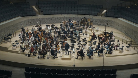 Musikerinnen und Musiker schauen auf die leeren Plätze der Bratschen im NDR Elbphilharmonie Orchester während einer Probe in der Elbphilharmonie. © NDR Foto: Screenshot