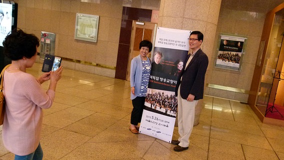 Zwei Konzertbesucher in Seoul lassen sich vor einem Konzertplakat fotografieren.  