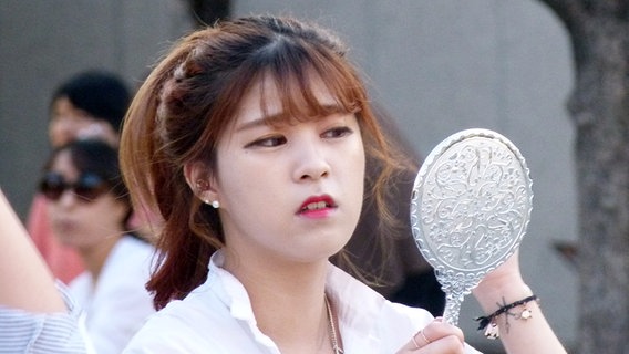 Eine junge Koreanerin schminkt sich draußen mit einem Handspiegel.  