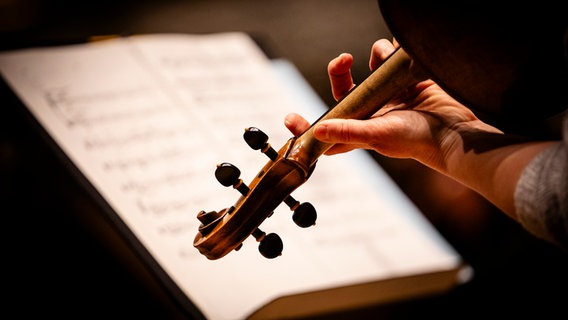 Die Schnecke einer Geige, dahinter ein Notenständer mit Notenblättern drauf © NDR Foto: Andy Spyra