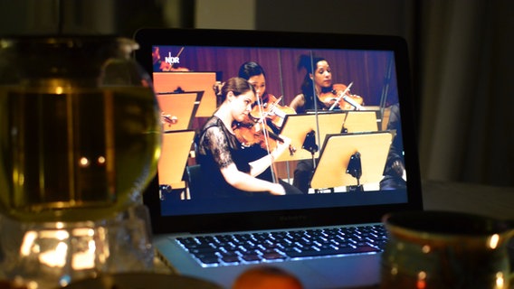 So könnte es aussehen beim Sofakonzert der NDR Radiophilharmonie: Der Video-Livestream läuft auf dem Laptop, dabei stehen Tee und Kerzen © NDR Foto: Stockmann-Productions