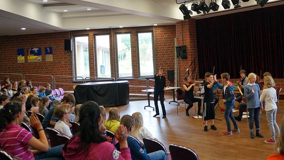 Beim Schulkonzert: Kinder spielen Klatschspiele auf der Bühne. Im Hintergrund ein Streichquartett  Foto: Wito Gasthaus