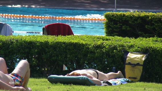 Eine Person sonnt sich auf der Liegewiese im Freibad. © Screenshot 