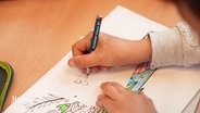 Ein Kind schreibt etwas auf ein Blatt Papier. © Screenshot 