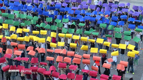 Luftbild: Menschen auf dem Rathausplatz halten bunte Plakate nach oben, sodass sie eine Regenbogenflagge bilden. © Screenshot 