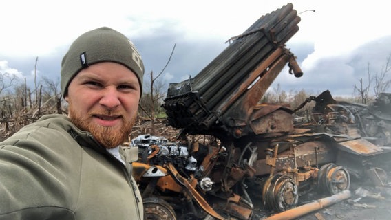 Der Ukrainer Eugen steht in Militärkleidung an der Front vor einer zerstörten Abschussrampe für Granaten. © privat 