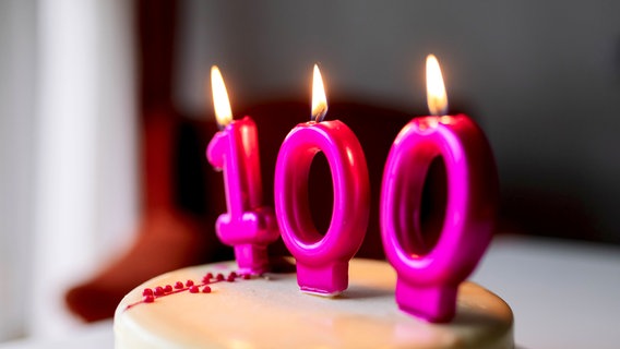 Auf einer Torte brennen Kerzen in der Form der Zahl 100. © photocase Foto: Addictive Stock