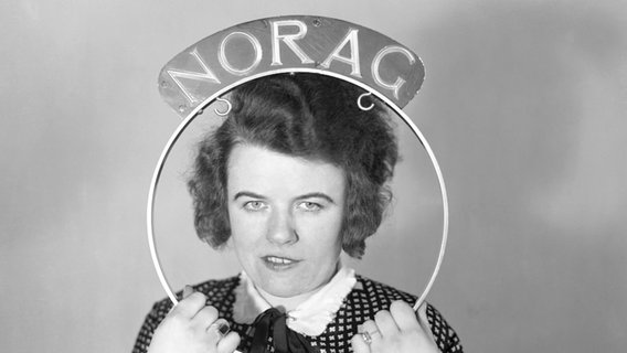 Ein Frau hält einen Bügel mit der Aufschrift Norag an ihren Kopf. © Screenshot 
