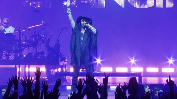Sänger Jared Leto steht auf einer Bühne und singt, im Hintergrund spielt ein Schlagzeuger. © Screenshot 