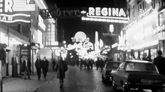 Historische schwarz-weiß Aufnahme. Passanten und Autos unter leuchtenden Neonschildern auf der Großen Freiheit. © Screenshot 