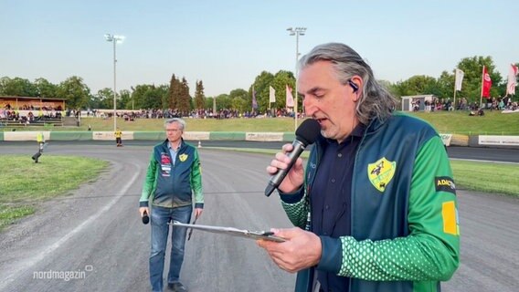 Motorsport-Arena-Sprecher Steffen Schulz mit einem Mikrofon neben der Rennstrecke beim Bundesliga Derby in Güstrow. © Screenshot 