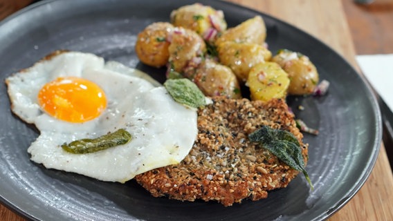 Knusperschnitzel vom Schwein mit Kartoffeln und Spiegelei auf einem Teller serviert. © NDR Foto: Florian Kruck