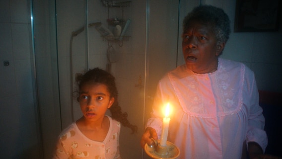 Amy (Melody Rose) und Tante Gordy (Elizabeth Clarke Hasters) gehen nachts mit einer Kerze in der Hand den seltsamen Geräuschen im Haus auf die Spur. © NDR/Letterbox 