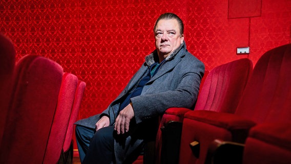 Ein Mann mit dunklere Kleidung (Peter Kurth) sitzt in einem roten Theatersessel und hat die Hand aufgelehnt © picture alliance/dpa | Christoph Soeder Foto: Christoph Soeder