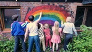 Sechs Kinder sprühen einen Regenbogen an eine Hauswand. © NDR.de 