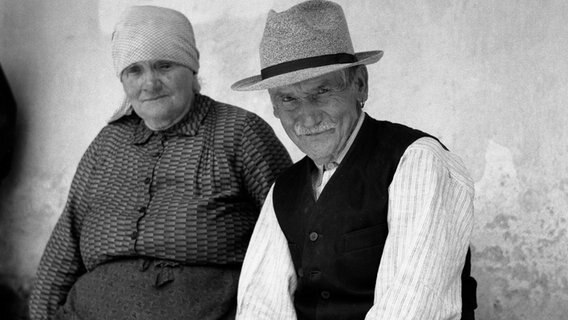 Altes Ehepaar sitzt auf einer Bank und schaut in die Kamera. © picture alliance / Agentur Voller Ernst | Agentur Voller Ernst / Hermann Fuss Foto: Hermann Fuss