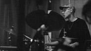 Ein Schwarz-Weiß-Foto von einem Schlagzeug spielenden Mann. © Anna Powell Denton Foto: Anna Powell Denton