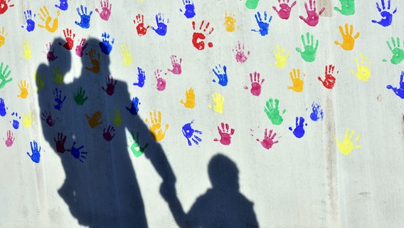 Der Schatten von Vater und Kind fällt auf eine bunt mit Händen bedruckte Wand © dpa-Bildfunk Foto: Peter Kneffel/dpa