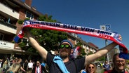 Ein Fan Fan des Verein Holstein Kiel stehen auf der Straße und präsentiert seinen Fanschal. © NDR Foto: NDR Screenshot