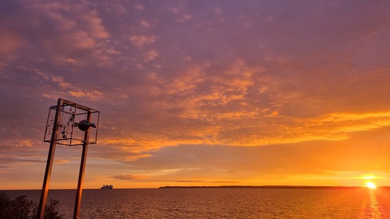 Ein Windspiel vor dem Wasser bei Sonnenuntergang. In der Ferne ist ein Schiff zu sehen. © Henning Dierken Foto: Henning Dierken