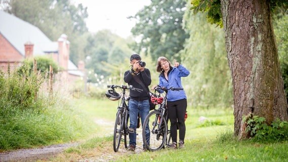Zwei Radfahrer stehen auf einem Weg vor dem Schloss Ludwigsburg in Vorpommern, der eine macht ein Foto. © TMV/Krauss 