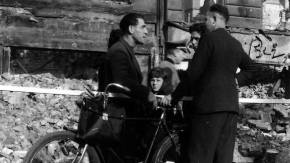 Zwei Männer und ein Kind stehen nach den Luftangriffen auf Hamburg 1943 in einer Straße voller Trümmer © Uwe Petersen Foto: Andreas Werner