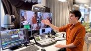 Ein Mann steht in einem Sendestudio und zeigt auf einen Bildschirm. © NDR Foto: Marco Peter