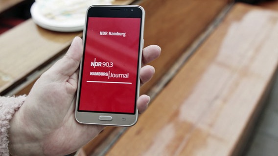 Screenshot: Eine Person hält ihr Smartphone so, dass darauf die Hamburg App von NDR 90,3 und dem Hamburg Journal zu sehen ist. © NDR Foto: NDR
