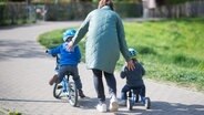 Eine Mutter geht mit zwei Kindern auf kleinen Fahrräden spazieren. © picture alliance Foto: -