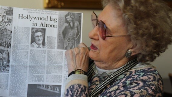 Helga Bischoff hält einen Zeitungsartikel, der mit "Hollywood lag in Altona" betitelt ist. © NDR Foto: Maxi Schmeißer