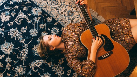 Miu liegt auf einem Teppich und hält eine Gitarre im Arm © Miu Foto: Zaucke