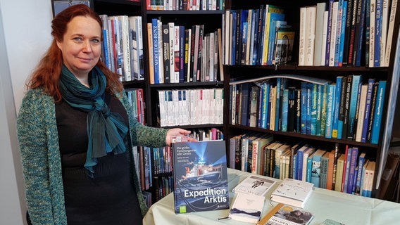 Buchhändlerin Maike Fuchs steht vor einem Büchertisch und präsentiert ein Buch. © NDR Foto: Kerstin von Stürmer