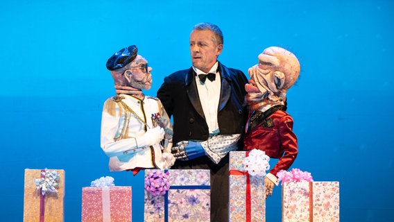 Ein Puppenspieler von der Gruppe Cipolla trägt links und rechts zwei Figuren mit großen Gesichtern. © Altonaer Theater Foto: G2 Baraniak