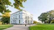 Ein weißes, klassizistisches Haus, das Jenischhaus,  im Sommer auf der grünen Wiese im Jensichpark. © Stiftung Historische Museen Foto: Sinje Hasheider