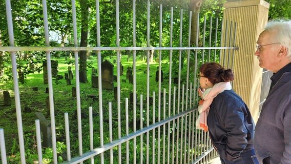 Eine Frau ( Ainhoa Montoya vom Stadteilkulturzentrum Wandsbek ) und ein Mann ( Stefan Romey vom Stadtteilprojekt "Jüdisches Leben in Wandsbek" stehen am Zaun zu einem Friedhof © Peter Helling Foto: Peter Helling