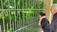 Eine Frau ( Ainhoa Montoya vom Stadteilkulturzentrum Wandsbek ) und ein Mann ( Stefan Romey vom Stadtteilprojekt "Jüdisches Leben in Wandsbek" stehen am Zaun zu einem Friedhof © Peter Helling Foto: Peter Helling