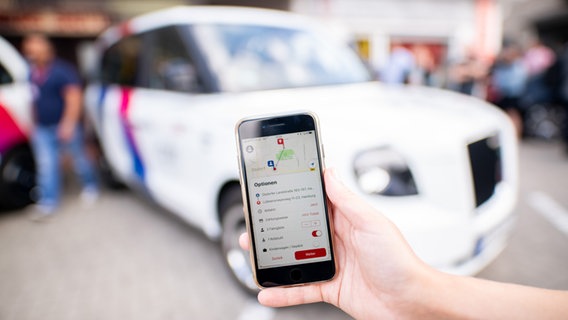 Eine Frau hält ein Smartphone mit der ioki-App vor ein Shuttle-Fahrzeug. © picture alliance/dpa Foto: Daniel Reinhardt