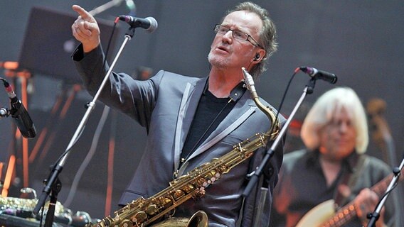 John Helliwell steht mit Saxofon auf der Bühne bei einem Supertramp-Konzert und zeigt ins Publikum. © picture alliance / dpa Foto: Oliver Krato