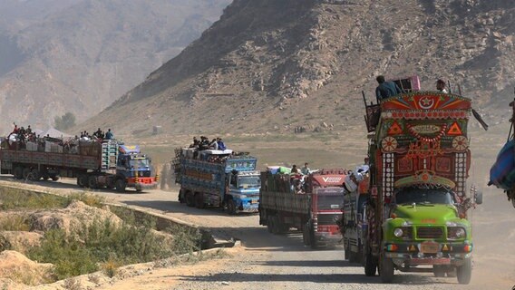 Lastwagen, auf denen afghanischen Familien sitzen, fahren zu einem Grenzübergang. Mit Beginn der geplanten Massenabschiebungen von Flüchtlingen in Pakistan drängen sich Tausende von Menschen an die Grenze zu Afghanistan. Die pakistanische Regierung hatte kürzlich angekündigt, Flüchtlinge ohne Aufenthaltsstatus ausweisen zu wollen. © picture alliance/dpa/AP | Muhammad Sajjad Foto: Muhammad Sajjad