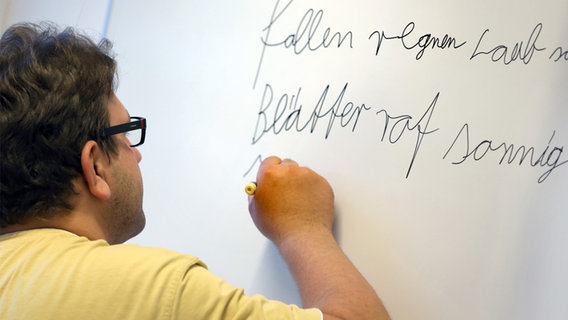 Ein erwachsener Schüler schreibt Wörter mit einem Stift an eine Kunststofftafel. © picture alliance / ZB Foto: Bernd Wüstneck