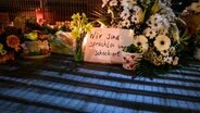 Blumen und Kerzen liegen und stehen im Stadtteil Alsterdorf vor dem Eingang zu einer Kirche der Zeugen Jehovas. © dpa Foto: Jonas Walzberg