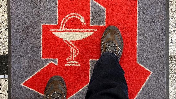 Mann geht über einen Teppich mit Apotheken-Logo © dpa Bildfunk Foto: Jens Büttner