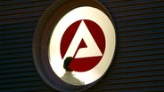 Hinter einem Fenster mit dem Logo der Agentur für Arbeit steht ein Mann im Treppenhaus. © picture-alliance/ dpa Foto: Franz-Peter Tschauner