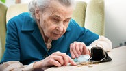 Eine Seniorin sitzt am Tisch und schaut nachdenklich auf ein wenig Geld und eine Geldbörse. © Fotolia Foto: Alexander Raths