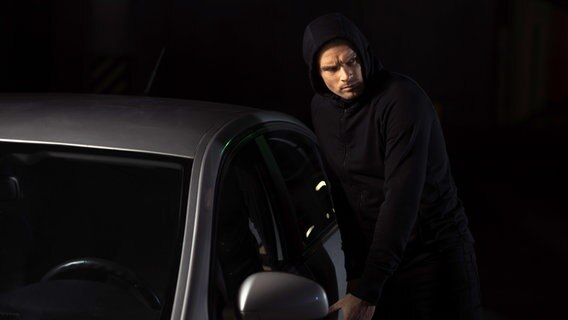 Ein schwarz gekleideter Mann bricht in ein Auto ein. © Colourbox Foto: -