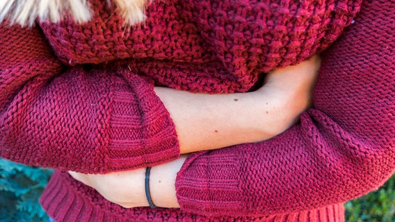 Eine von oben betrachtete Frau im roten Pullover, hält sich mit beiden Händen den Bauch. © fotolia.com Foto: animaflor