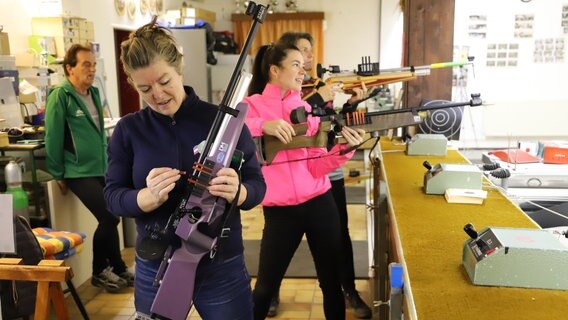 Mutter Christiane lädt das Gewehr nach, während Tochter Francesca bereit für die Zielscheiben ist. Vater Hans-Peter beobachtet den Ablauf im Hintergrund. © NDR Foto: Marina Heller