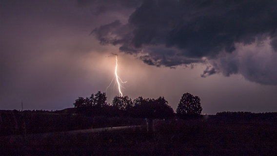 Ein Blitz schlägt auf einem Feld ein, eine dunkle Wolke zieht über den Himmel. © Photocase Foto: salvia77