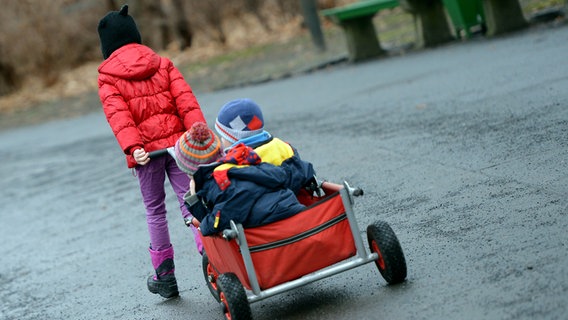 Ein Mädchen zieht zwei weitere Kinder in einem Bollerwagen. © picture alliance / dpa Foto: Britta Pedersen